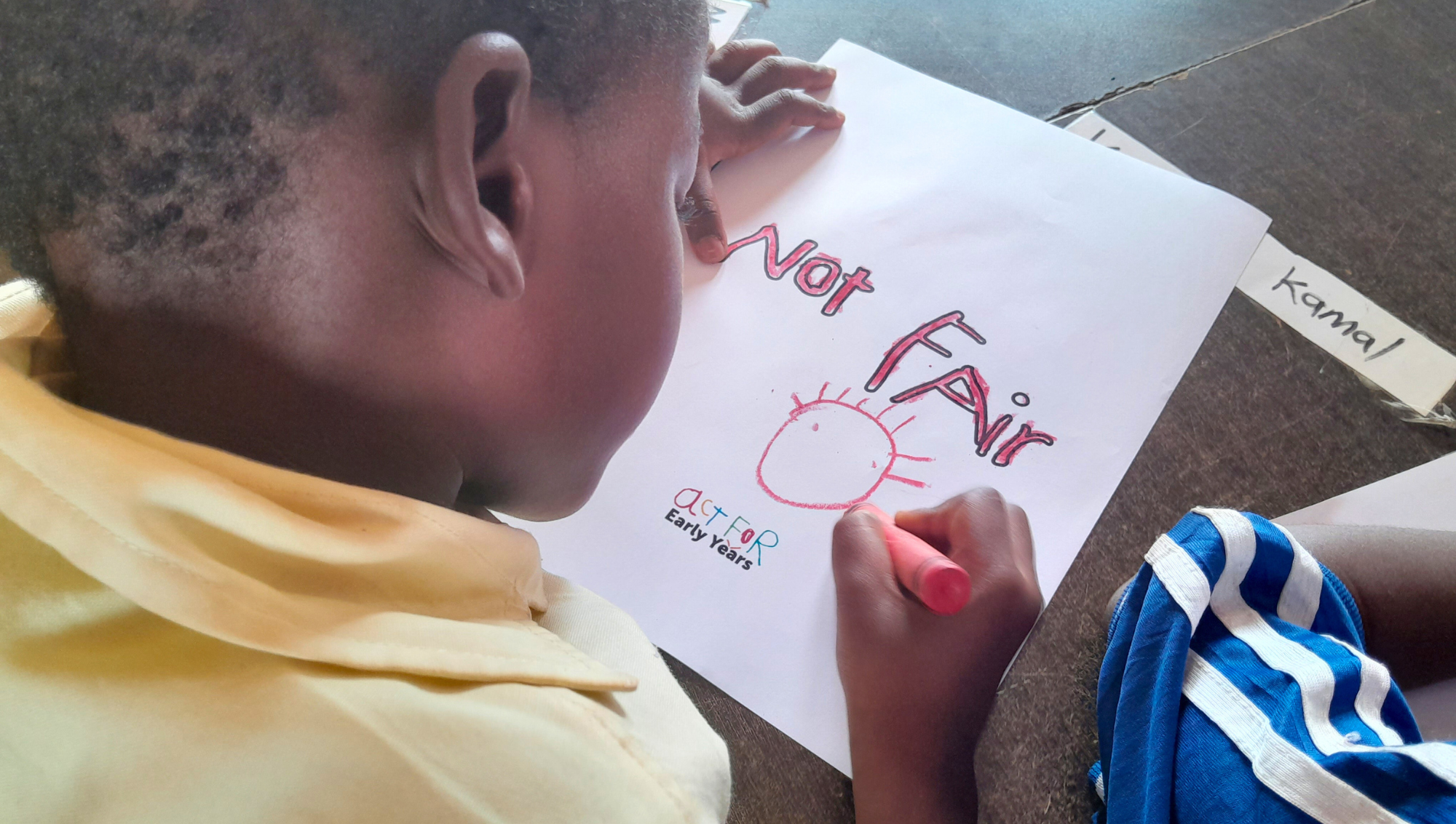 A child colours in 'No Fair' on an Act For Early Years campaign poster