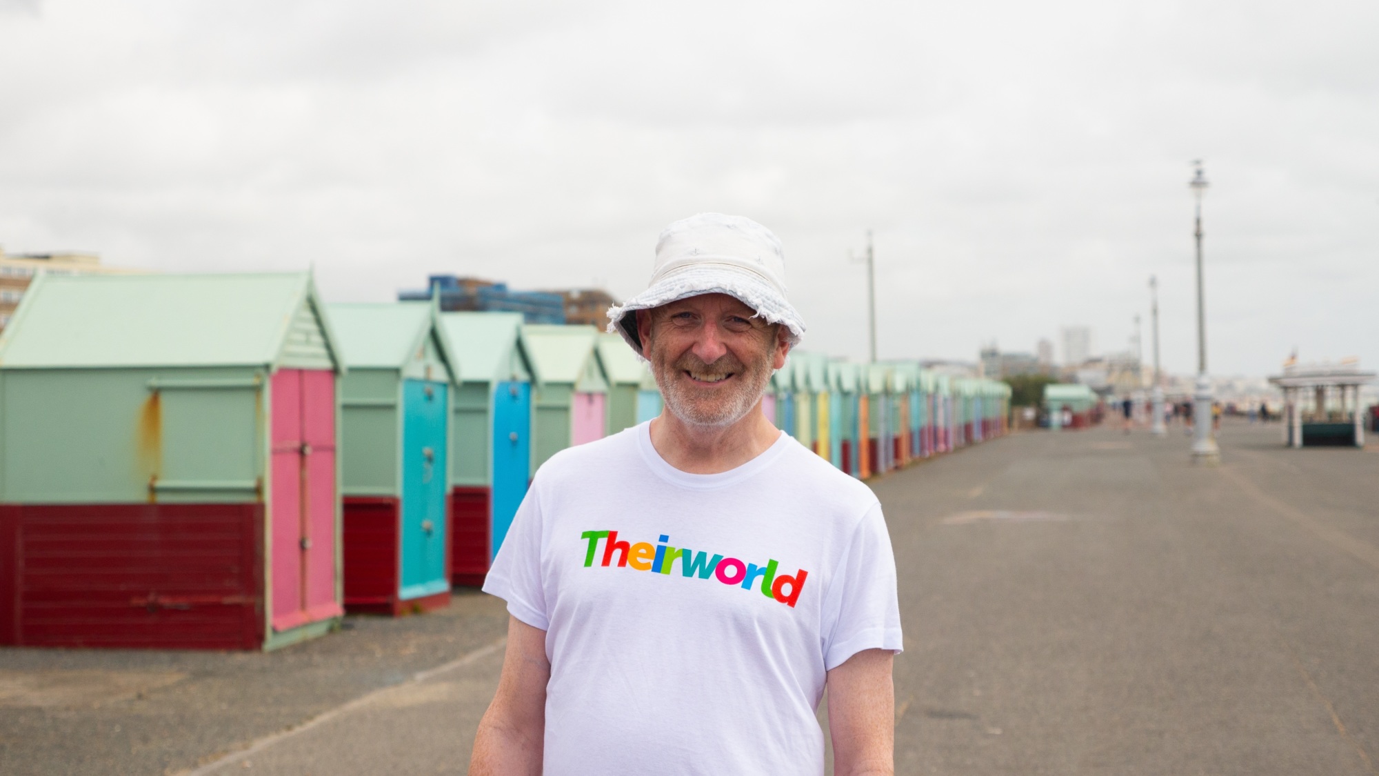 Nick Sharratt stands on Brighton seafront with brightly coloured huts behind him