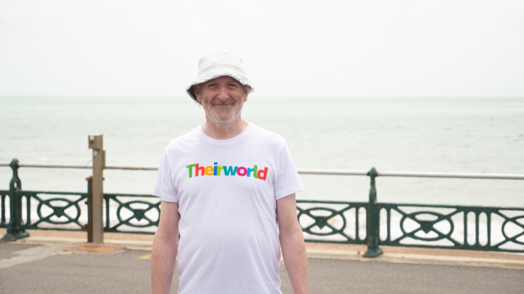 Nick Sharratt stands on Brighton seafront wearing a Theirworld t-shirt