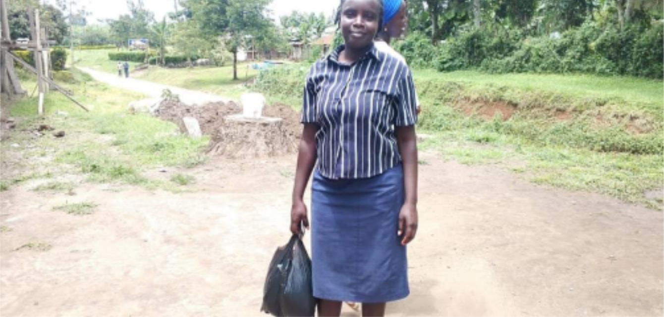 Teenage mother stands on a dirt road and smiles at the camera