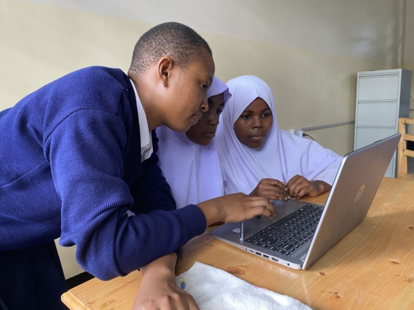 Three students gather around a laptop